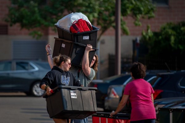 One person holds a plastic bin while another hoists up two bins full of belongings.