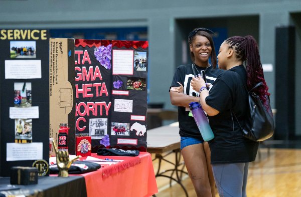 Two people talk in front of a display on a table about a sorority.