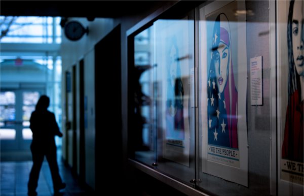 A person passes by the Becoming America: Our Past, Present, and Future at 250 art exhibit in the Lake Ontario Hall Wall Gallery on January 9. Pictured at right is a series of three screenprint portraits entitled &#8220;We the Future&#8221; by Shepard Fairey.