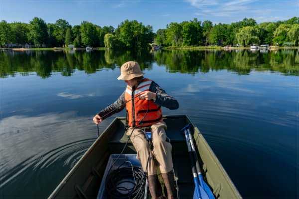 A person sitting at the end of a boat dropping a line down into the lake.