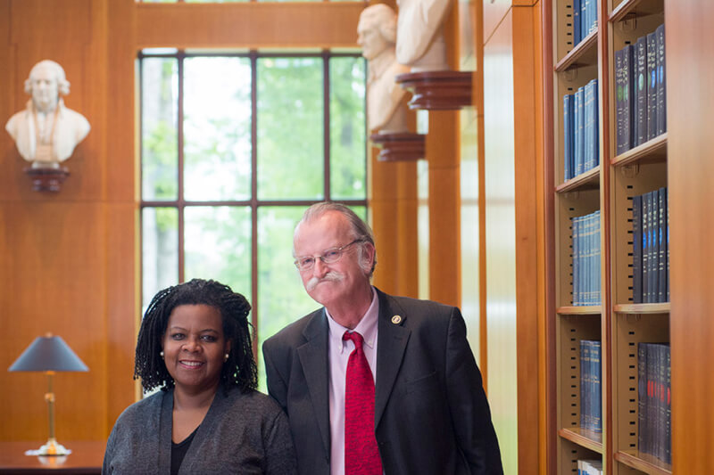 Annette Gordon Reed and Peter Onuf stand, smiling, side-by-side in a room with books on shelves on the right wall, There is a window in the background.