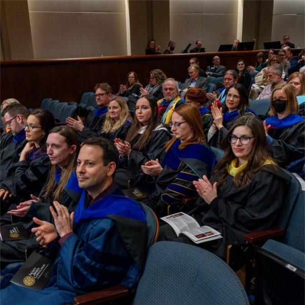faculty in academic regalia applauding from auditorium seats
