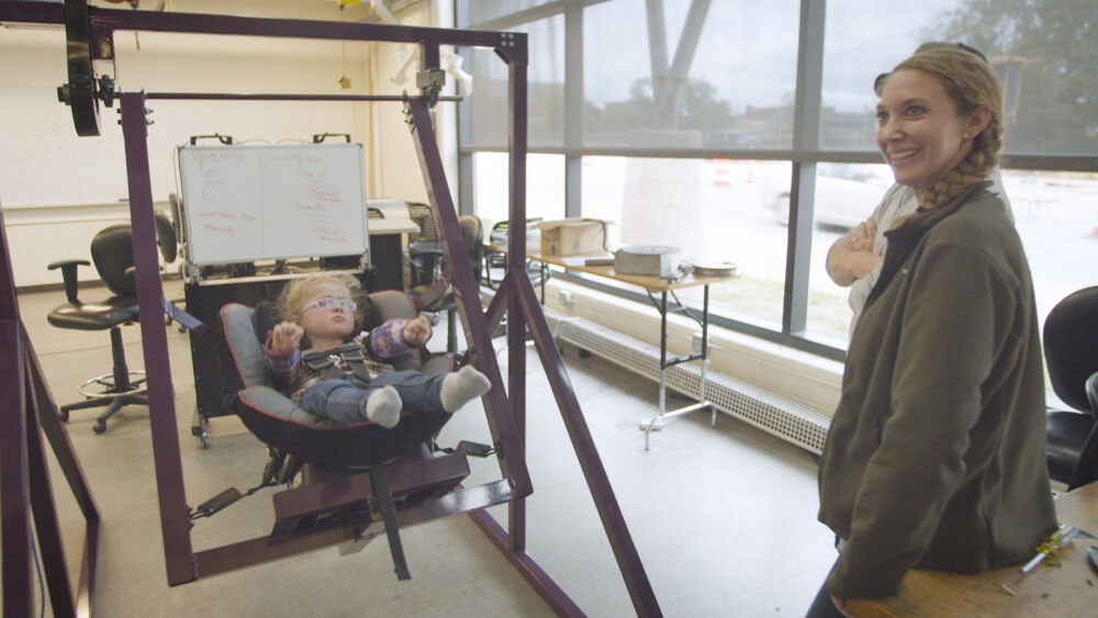 Sarah Truax, right, smiles as her daughter, Alexis, rides in a custom-built swing made by Grand Valley engineering students.