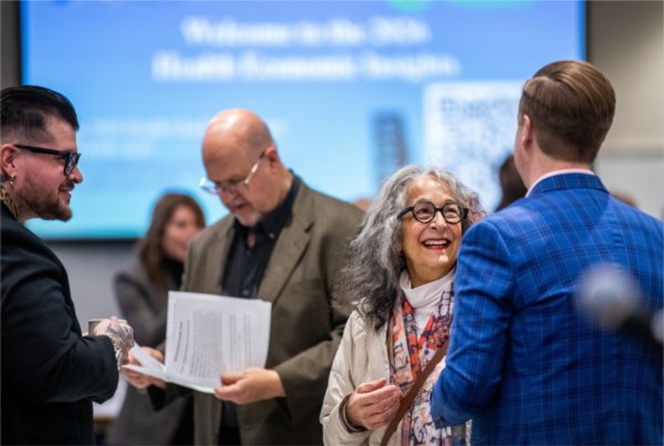 Diana Lawson stands talking to someone in a blue jacket, people stand behind her