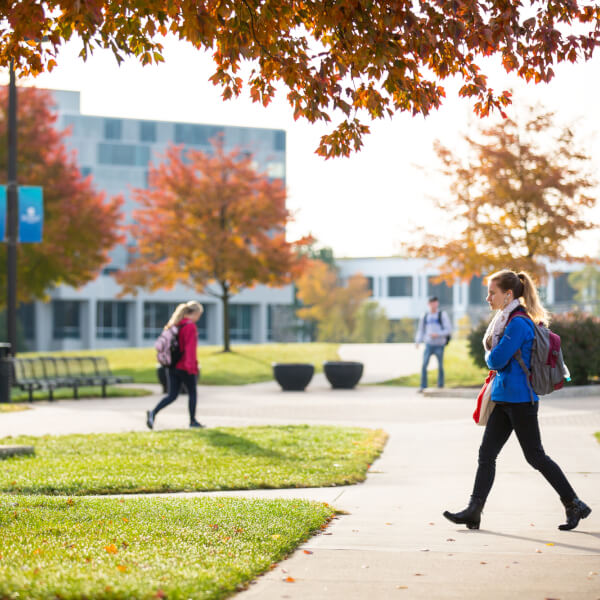 A student walks down a sidewalk near the clock tower on the Allendale Campus. Zumberge pond is in the background.