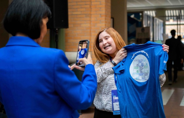 President Mantella takes a picture of a person from Human Resources showing off a Reach Higher T-shirt.