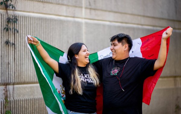 Students Jackelyn Palmas and Jose Medina laugh with one another, holding onto Mexican flags. 