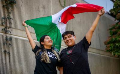 Students Jackelyn Palmas and Jose Medina stand next to each other, each holding a corner of the Mexican flag, which flies behind them.