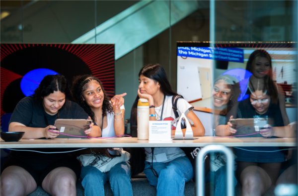 Three young women sit at a table in the Technology Showcase and play with a program controlled through an iPad.
