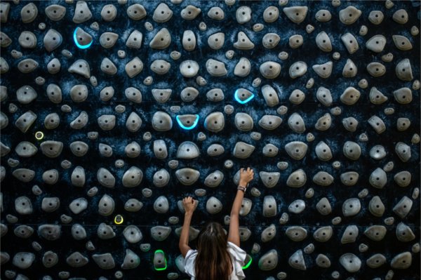 A person climbs a rock wall where a few select rocks are lit up blue.
