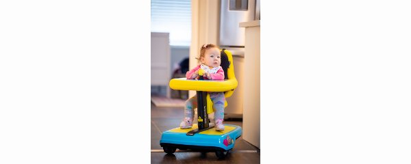 blue and yellow mobility device with toddler seated in it, in a home or office setting