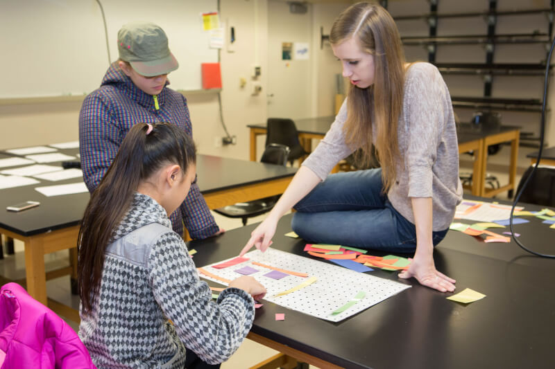 Grand Valley student Katrina Teunis helps middled school students find the solution to a mathematical puzzle.
