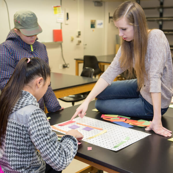 Grand Valley student Katrina Teunis helps middled school students find the solution to a mathematical puzzle.