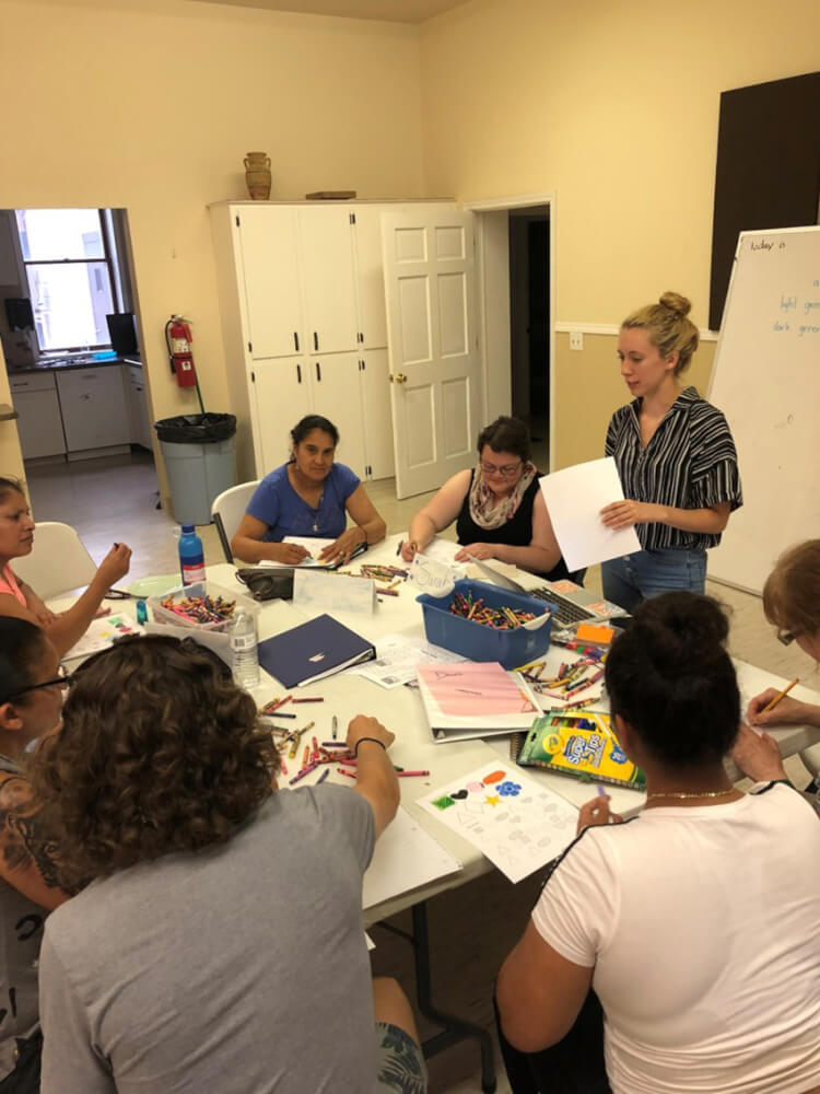 women standing at table talking with adults who are seated