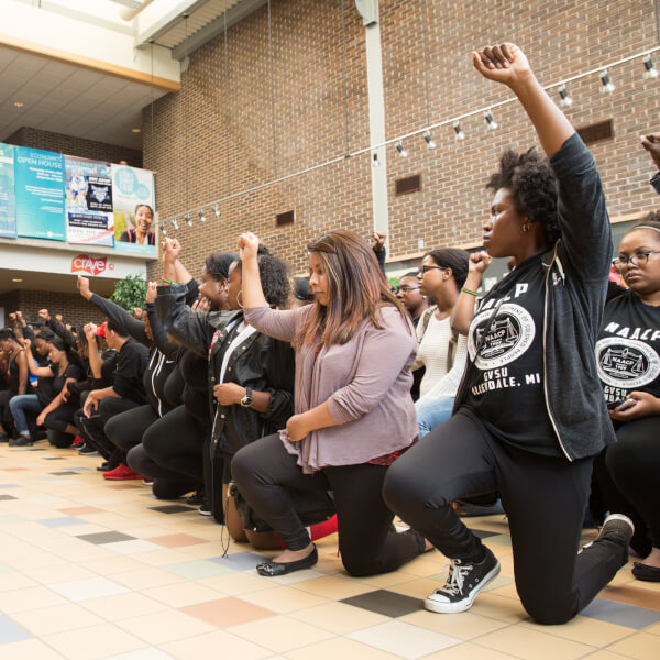 Photos by Amanda Pitts.  Students kneel with fists raised in the Kirkhof Center prior to holding a justice rally at the Cook Carillon Tower. Antoinette Jackson, NAACP chapter president, is at left.