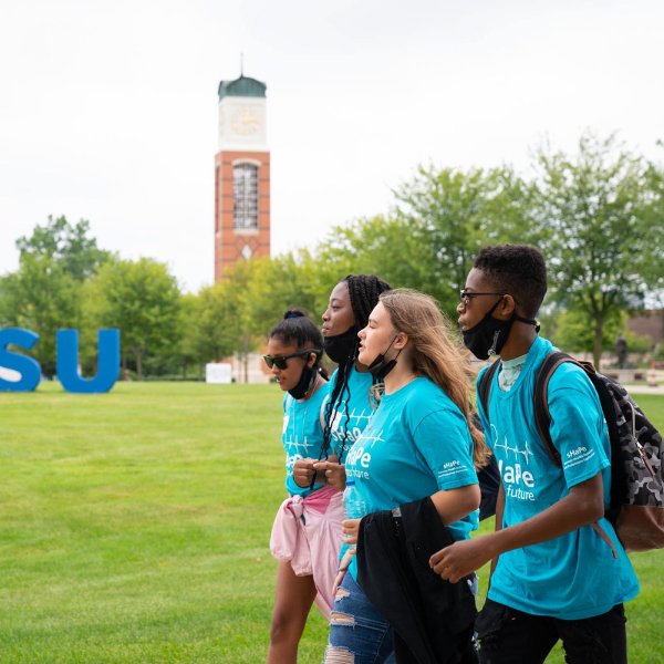four students walking in front of Cook Carillon Tower and letters GVSU on lawn