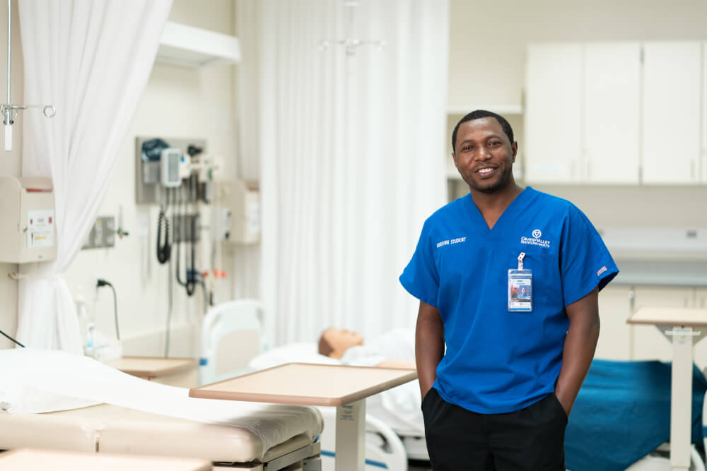 Jackson Byiringiro, in nursing scrubs, standing in the simulation center