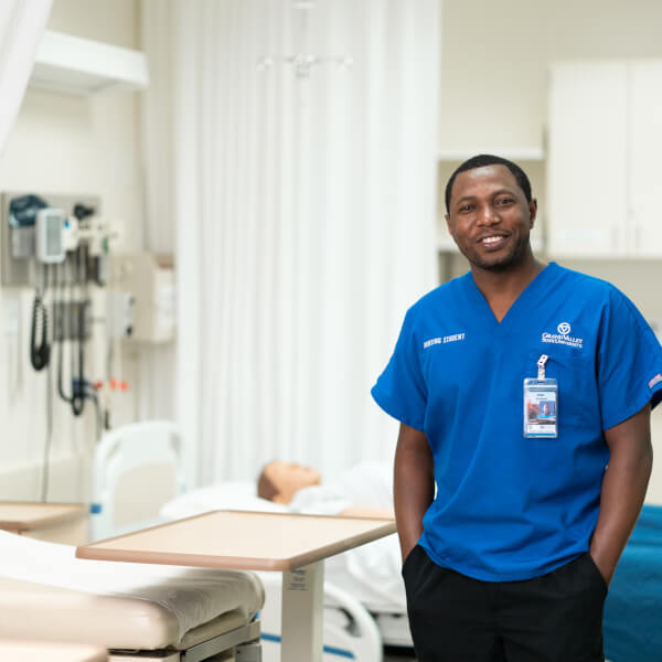 Jackson Byiringiro, in nursing scrubs, standing in the simulation center