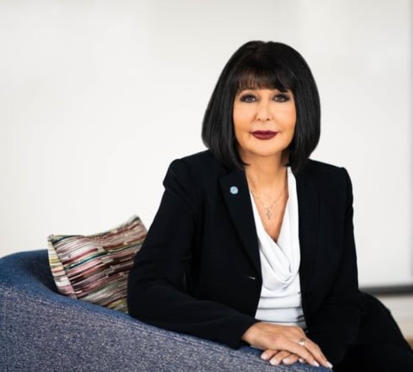 A person sits in a chair with hands folded on the arm of the chair for a posed photo.