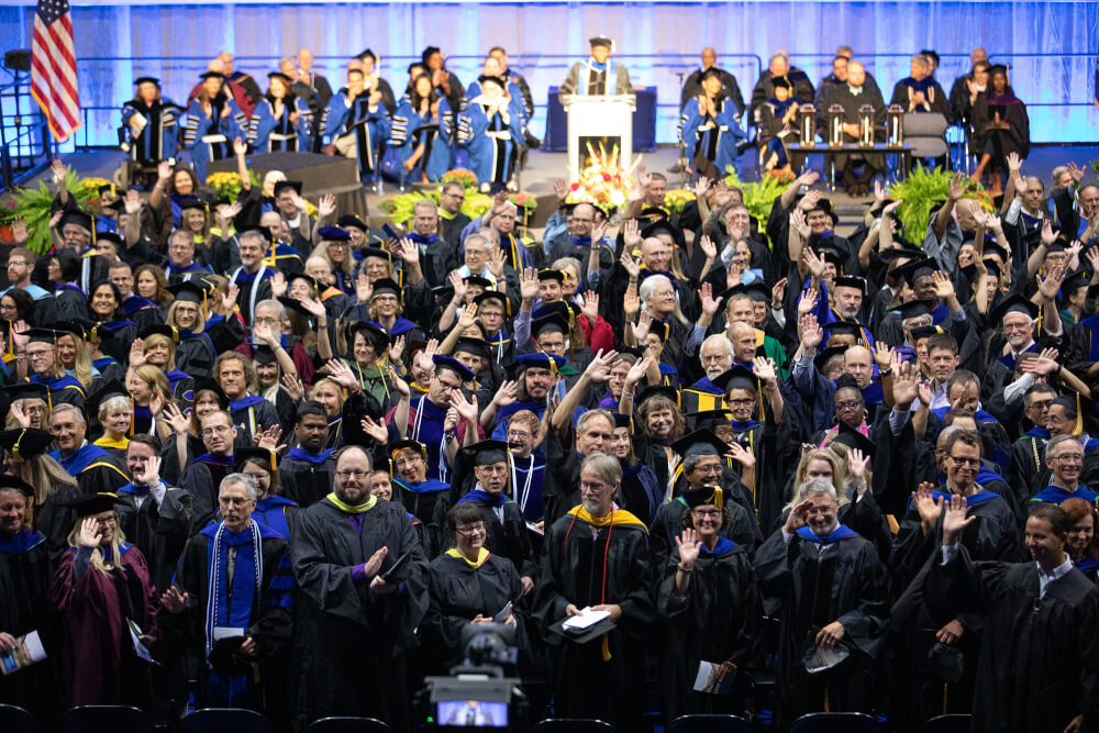 faculty in regalia waving to students