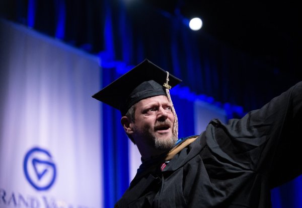 A person wearing a cap and gown looks at the audience over their shoulder.