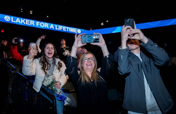 People smile while holding up phones. The words "Laker for a Lifetime" are in the background.