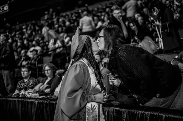 A person kisses the cheek of another person who is wearing graduation garb.