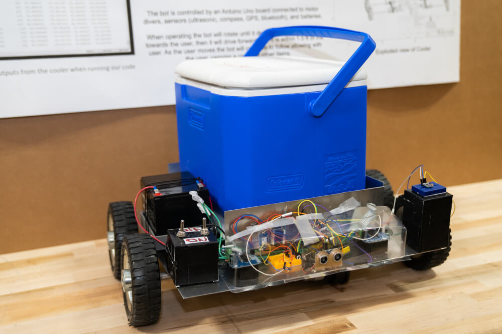 A blue cooler sits on a metal frame bearing wheels, which the robot uses to roll around, following its owner.