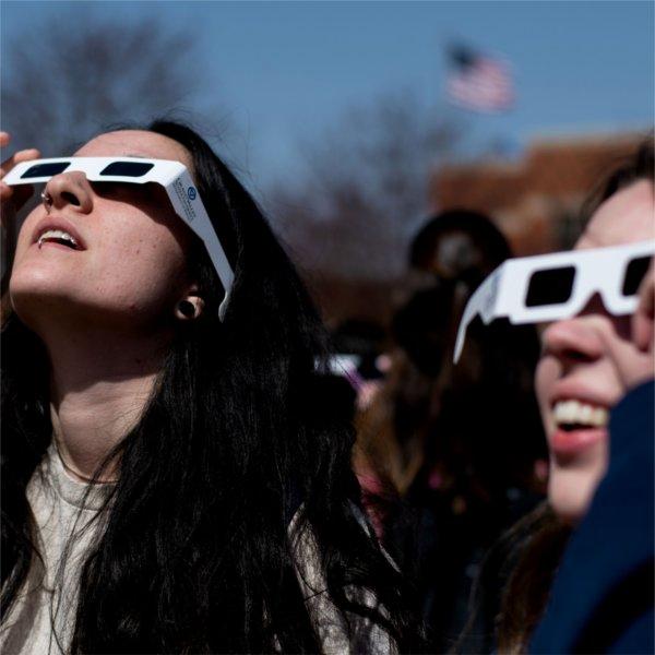 Two people wearing special glasses for a solar eclipse look skyward.