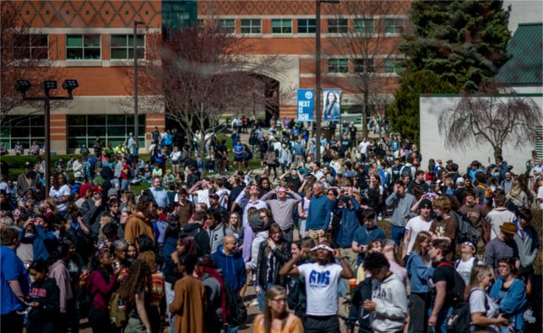 A large group of people, some of them wearing special glasses for a solar eclipse, gather on the Allendale Campus.
