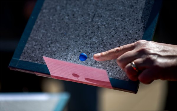 The index finger on a person's hand points to a small blue ball next to a pink card.
