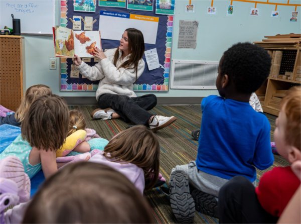 Bailey LoFiego reads a book to young children seated on the floor