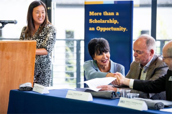 GVSU President Philomena V. Mantella shakes hands with Grand Rapids Community College Interim President Steven Triezenberg. Pink hug at the podium.