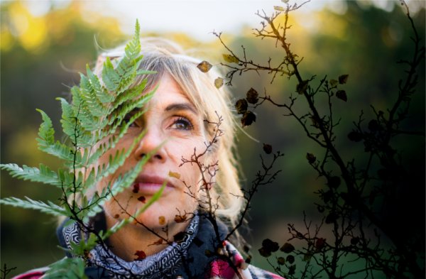 A person looks into the distance with a leaf and some brown branches in the foreground.
