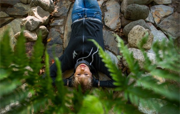 A person looks up while lying on stone. Plants are in the foreground.