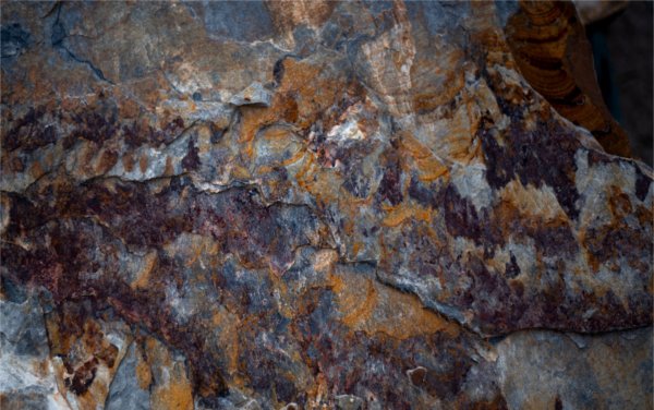 A closeup of rock with different color striations, including gray, white, rust and brown.