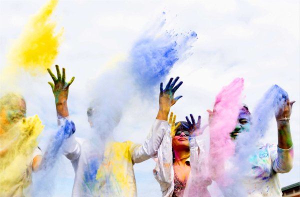 People smile and laugh as hands toss colorful powder dust into the air to celebrate holi festival. 