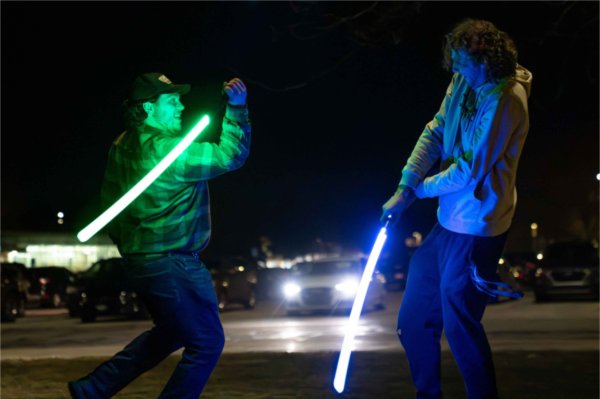  Two college students use blue and green light sabers as they pretend fight. 
