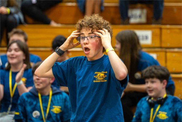  A middle school student wearing glasses and a blue shirt shows an expression of surprise when hearing he won an award. 