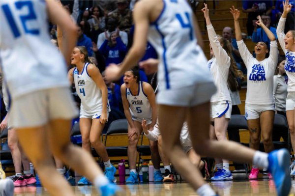Women's basketball team erupts in excitement from the bench as a teammate makes a three-pointer. 