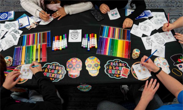 Hands work on dio de los muertos coloring sheets with colorful pencils. 
