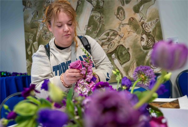 A college student arranges purple flowers.  