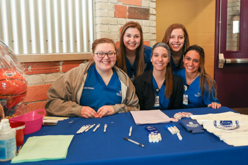 Five women nursing students sitting and posing behind a table.