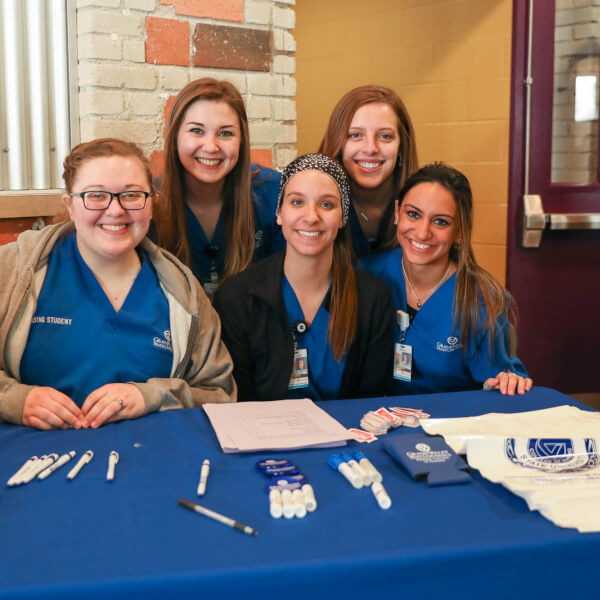 Five women nursing students sitting and posing behind a table.