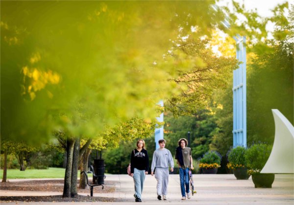  Three college students walk past changing leaves on a college campus. 
