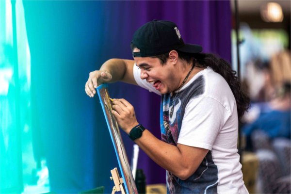  A person wearing a black hat laughs as they do art work. 