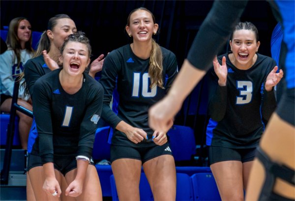  Three women's college volleyball players react during a game. 