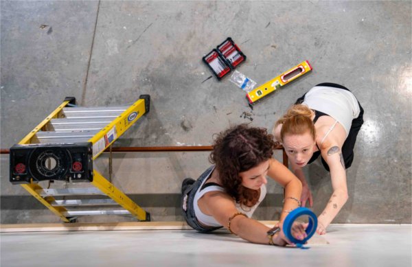  Two college students work with ladders, tape and a level to help on an art installation. 