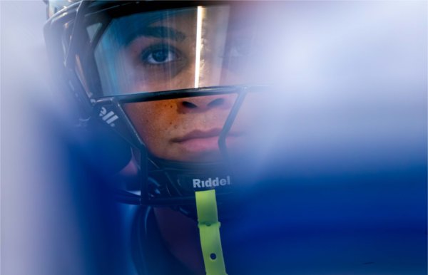   A football player's face is seen through a blue haze of a huddle. 