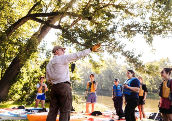 A professor gestures to students about to embark in kayaks on a river. 